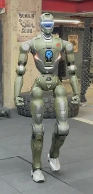 The EngineAI T800, a full-size humanoid robot in olive-green armored plating, walking through a boxing gym